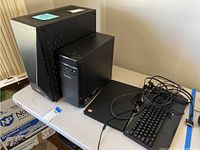 Two black desktop towers side by side on table with keyboard and cables