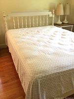 Overall front view of painted wood spindle headboard and frame with sheet-covered mattress