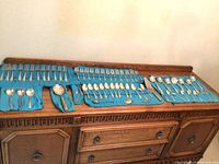 Full display of Birks Regency flatware laid out on a wooden sideboard with a blue cloth roll organizer. Shows multiple forks, spoons, knives, and serving pieces.
