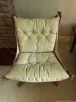 Front view of the chair showing tufted canvas seat and back cushions, wooden X-base and leather strap attachments