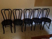 Six black bentwood chairs lined up in a room showing their curved backs and legs.