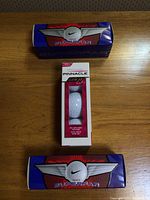 Three boxes of golf balls on a wooden table: two Nike Superfar blue boxes with red and white logo, one white Pinnacle Gold Lady box with single ball visible.