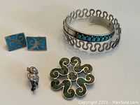 Sterling silver bracelet with turquoise stones, blue and silver rectangular cufflinks, green stone brooch, and figurine pendant all displayed together