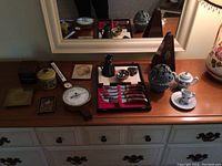 Wide view of items arranged on wooden dresser showing metronome, steak knife set, pitcher, marbles, decorative sphere, teacups, boxes, and framed art.