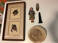 Overview photo showing the framed woven portraits, the three small figurines, and the round stone plaque.