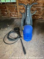 Full view of Simoniz pressure washer showing blue main body and attached hose and spray wand laid out on wooden floor.