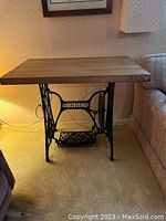 Front view of Singer sewing machine base table with wooden top located next to sofa and lamp.