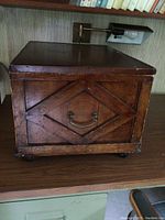 Front view showing wooden diamond trim and metal handle on storage box.