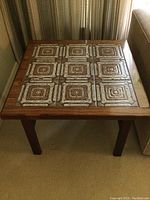 Front view of square wooden side table with nine ceramic tiles inset on the top surface showing patterns and wood frame.