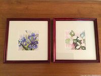 Pair of framed watercolour paintings, one with purple irises and one with pink and white flowers.