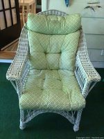 Front view of white wicker chair with green patterned cushioned seat and backrest, showing the seat cushion and back support.