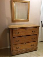 Wood cabinet with three drawers and metal handles, positioned under matching wood-framed mirror.