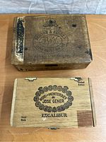Photo showing two vintage wooden tobacciana boxes with cigar branding, one dark aged wood with Daison & Hedges and one light wood with Jose Gener Excalibur branding.