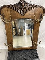 Front view of the antique wooden framed mirror with carved details and four brass hooks, shown standing upright.