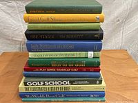 Photo shows a stack of 12 assorted golf books with various titles visible on their spines, arranged vertically against a white background.
