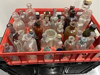 Photo showing collection of 39 old bottles of various shapes, sizes, and colors housed in a red plastic crate.