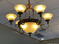 Chandelier lit, showing warm glowing frosted glass shades and ornate bronze frame