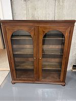 Front view of antique wooden curio cabinet with double glass doors and wooden shelves inside.