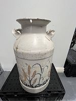 Front view of white metal milk can with painted wheat and grass design, showing handles and flared top.