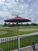 Patio umbrella set up outdoors showing full canopy, pole, rope and pulley mechanism, and base attached to railing.