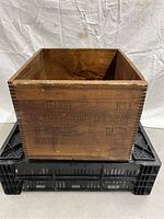 Photo of an old pine wooden box with stenciled black lettering related to distillery and liquid gallons, placed on a plastic crate.