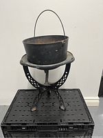 Photo of the black cast iron pot with handle placed on a black decorative cast iron stand with tripod base and cut-out design.