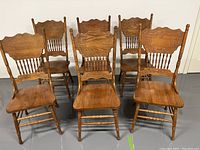 Six hardwood press-back chairs arranged in two rows on gray floor