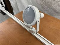 Close-up of one round white adjustable spotlight attached to a white track section, mounted on an adjustable bracket for directional lighting.