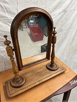 Wooden washstand mirror showing arched mirror held by two turned wooden supports on rectangular base.