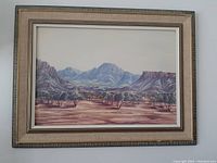 Full view of the framed landscape painting showing the desert landscape and mountain range in natural colors with trees and distant hills.