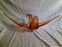 Front view of amber art glass sculpture on white fabric background showing extended wings and curving central form.