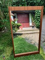 Full view of the rectangular Mid-Century Modern teak mirror placed outdoors, showing the wood frame and reflective surface.