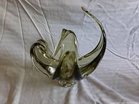 Side angle view showing the flowing curved design of the olive green art glass vase on white fabric background.