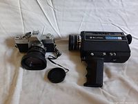 Minolta SRT 100 35mm camera next to Bell & Howell Filmosound XL movie camera on white surface.