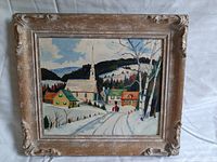 Vintage oil painting in a carved wooden frame showing a snowy village with houses, a church with steeple, hills, and trees.