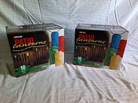 Two unopened boxes of Woods Patio Lanterns, featuring colorful tiki light covers, photographed on a white sheet background.