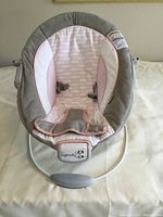 Full view of the Ingenuity baby bouncer seat showing padded seat in pink and gray fabric and front control panel for music and movement.