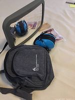 Photo showing the Britax baby car mirror with strap, blue toddler hearing protection earmuffs, soft grey carrying case, and packaged cardboard binoculars on a white surface.
