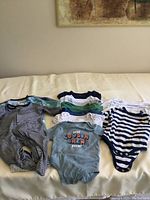 Photo showing an array of short sleeve baby onesies of various colors and prints, along with a few long sleeve, long leg striped onesies.