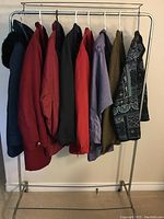 Eight women's jackets on a silver metal hanging rack with white plastic hangers, displayed from left to right.