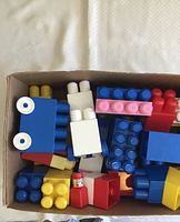 Box containing various colored Ritvik Mega Blocks and figure parts