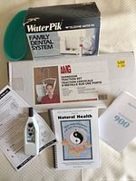 Photo showing Water Pik Family Dental System box, AMG Overdoor Traction unit box, Professional 900 Acuhealth TENS unit device with instruction sheets and booklets on a light-colored surface.