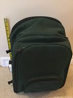 Green fabric backpack-style picnic knapsack standing upright with measuring tape showing height about 17 inches