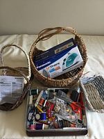 Boxed Panasonic steam iron placed inside large wicker basket alongside a metal tin with assorted sewing supplies such as threads, needles, pins, scissors
