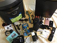 Full lot showing two paper shredders, cameras, speakers, cell phones, cords, and chargers arranged on floor near a white surface.