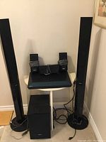 Sony BDV-E4100 surround sound system including receiver, subwoofer, two tall floor-standing speakers, and two small satellite speakers with cables attached, all positioned against a wall.