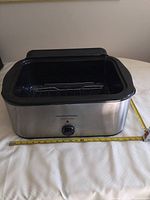 Front view of the Hamilton Beach roaster oven with temperature control knob and measuring tape showing width dimension.