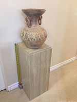 Full view of pottery urn on top of faux marble pedestal stand, showing approximate height with measuring tape