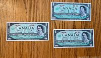Front view of three 1937 Canadian one dollar bills depicting Queen Elizabeth II, showing two crisp bills and one with some wear.