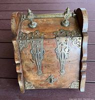 Top view showing wood finish, curved sides, and detailed brass hinges and finials on lid.